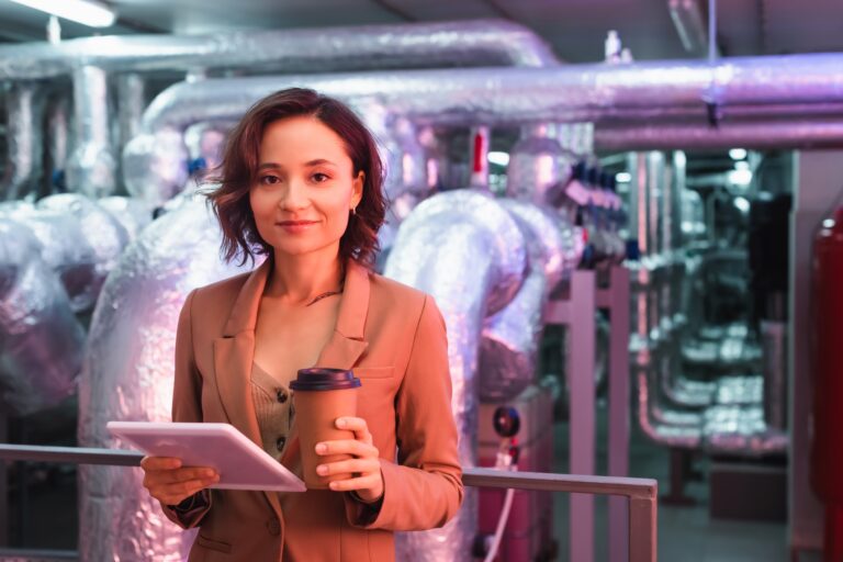 young engineer with digital tablet and coffee to go smiling at camera in technical room of data