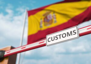 Barrier gate with CUSTOMS sign being closed with flag of Spain as a background. Spanish restricted border crossing or protective tariffs. 3D rendering