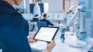 Engineer Holds Green Mock-up Screen Digital Tablet Computer. In the Background Team of Industrial Engineers Working with Functional Robot Arm in Modern Bright Research Facility